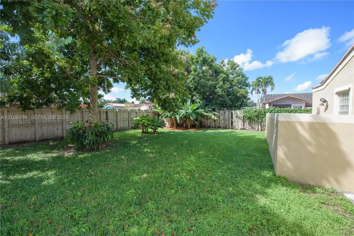 Backyard featuring a manicured lawn, perimeter wood fencing, mature trees, and an exterior masonry wall