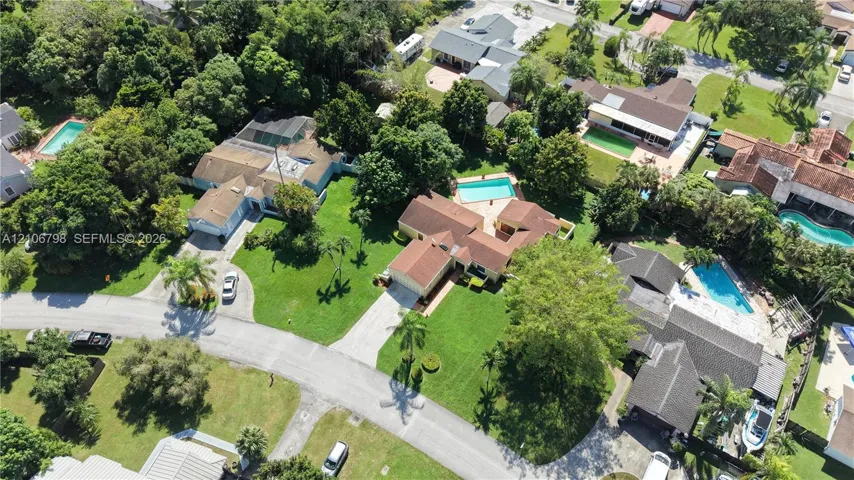 Aerial perspective of a multi-structure property featuring a pitched tile roof, expansive manicured lawn, concrete driveway, and a private swimming pool