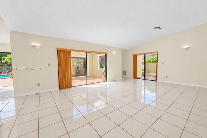 Spacious interior featuring vaulted ceilings, oversized ceramic tile flooring, dual sliding glass door systems, and wall-mounted sconce lighting