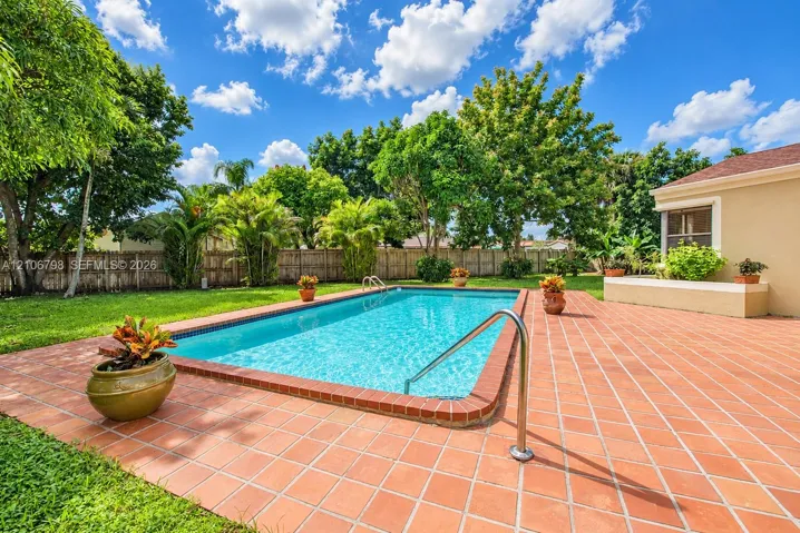 Rectangular swimming pool featuring a brick-tiled deck, metal handrail, and integrated raised masonry seating wall