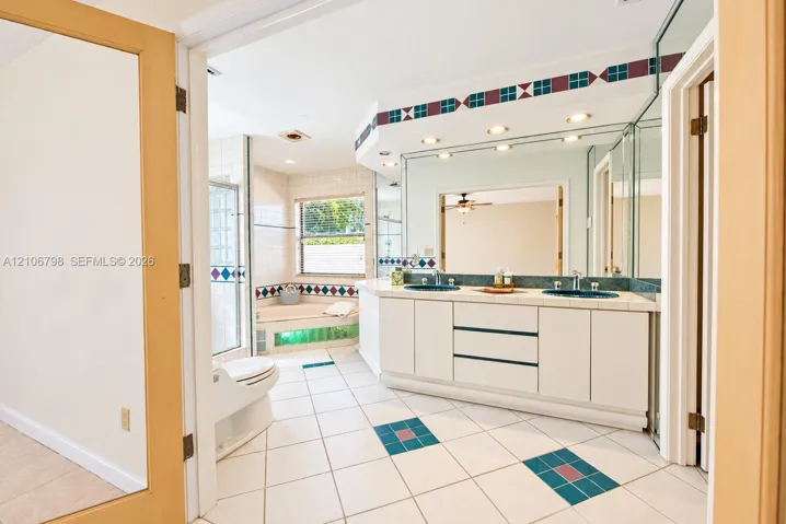 Bathroom featuring a dual-sink vanity with tile countertops, a soaking tub, recessed ceiling lighting, glass-enclosed shower, and decorative tile flooring