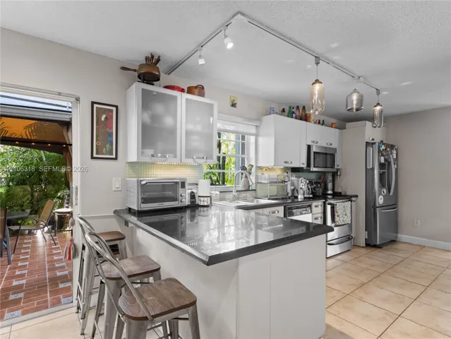 Kitchen featuring white cabinetry with glass-panel upper doors, dark stone-finish countertops, stainless steel appliances, and adjustable track lighting