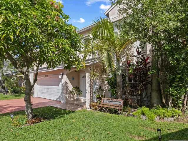 Two-story exterior featuring a stucco facade, an attached two-car garage with a sectional door, a covered entryway, and mature tropical landscaping