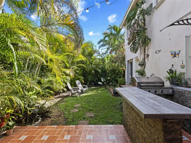 Outdoor patio featuring tile flooring, built-in stone-clad grill station with stone countertop, and mature palm landscaping