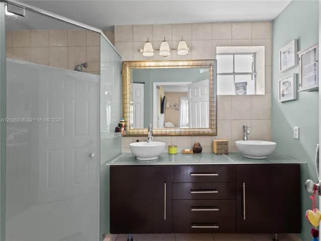 Floating vanity with a frosted glass countertop, dual white vessel sinks, polished chrome fixtures, and a framed wall mirror