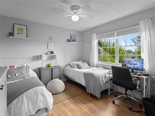 Wood-finish flooring, ceiling fan with integrated lighting, and multi-pane window with natural exterior foliage