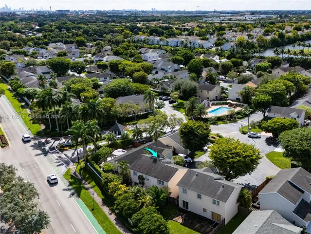 Aerial perspective of a multi-story residence featuring a shingled roof, light-toned exterior siding, mature landscaping, and an integrated private parking area