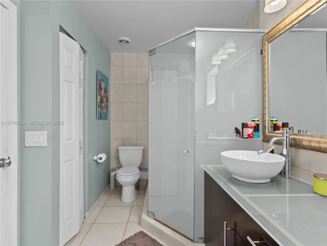 Vanity featuring a glass countertop and oval vessel sink, framed wall mirror, corner glass-enclosed shower, and tile flooring