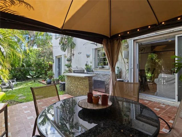 Outdoor living space featuring a built-in outdoor kitchen with stone veneer, stainless steel grill, tile patio flooring, and a permanent gazebo structure