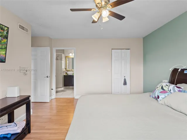 Bedroom featuring wood-finish flooring, a ceiling fan with integrated lighting, a dual-panel closet door, and an accent wall