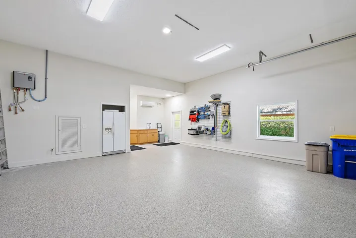Garage interior featuring speckled epoxy flooring, built-in cabinetry, a wall-mounted ductless heating and cooling unit, overhead lighting, and a window
