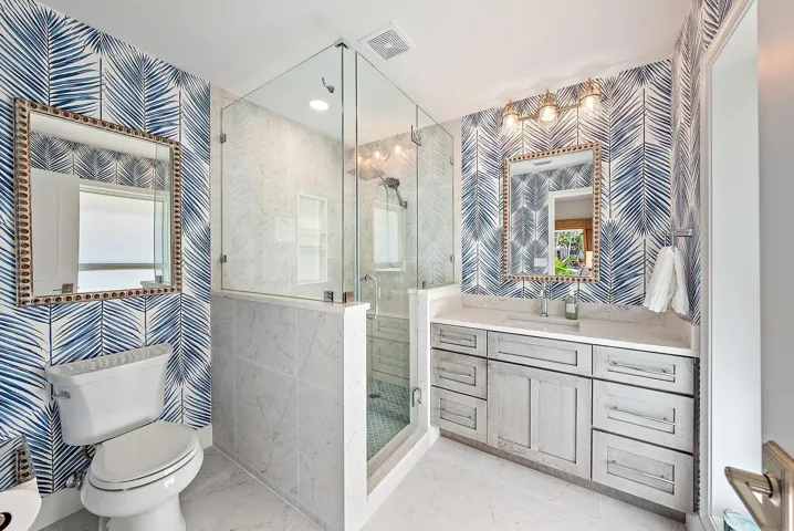 Bathroom featuring a glass-enclosed shower with stone-tile surround, custom wood-finish cabinetry, stone-top vanity, and dual wall-mounted mirrors with metallic trim