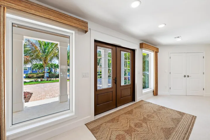 Double entry doors with divided-lite glass panels, neutral tile flooring, recessed ceiling lighting, and large picture windows featuring wood-finish valances
