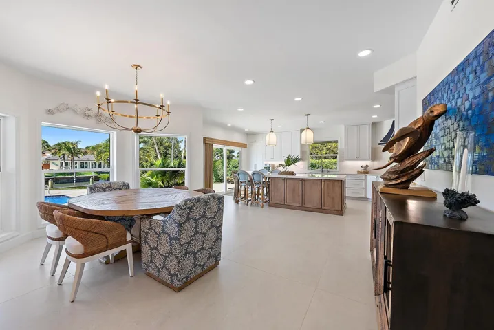 Open-concept kitchen and dining area featuring large-format tile flooring, a multi-tone kitchen island, white shaker-style cabinetry, and a circular metal chandelier