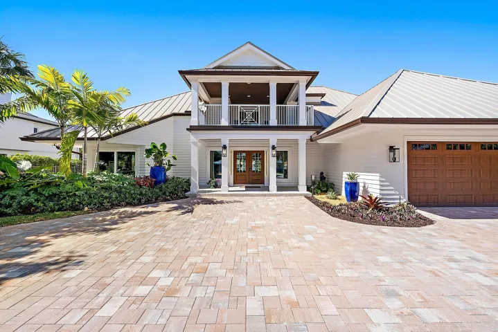 Two-story exterior featuring a metal roof, paver driveway, double-door entrance, second-story balcony, and multi-car garage with wood-finish door