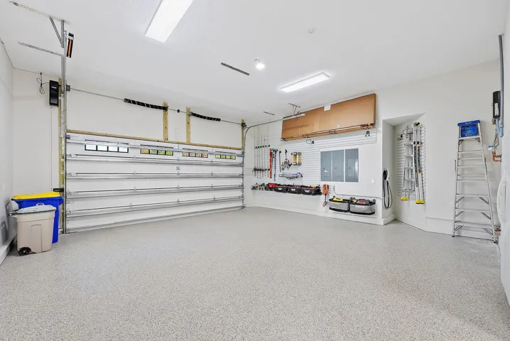 Spacious garage featuring an epoxy-coated floor, integrated wall-mounted slat board storage system, overhead fluorescent lighting, and a multi-panel sectional door