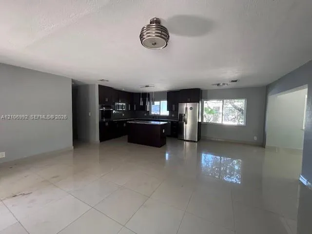 Kitchen featuring dark cabinetry, center island, stone-finish countertops, stainless steel appliances, and large-format tile flooring