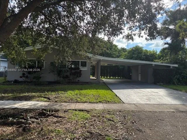 Single-story exterior featuring a low-pitch roofline, integrated carport, concrete driveway, and front lawn with mature canopy trees