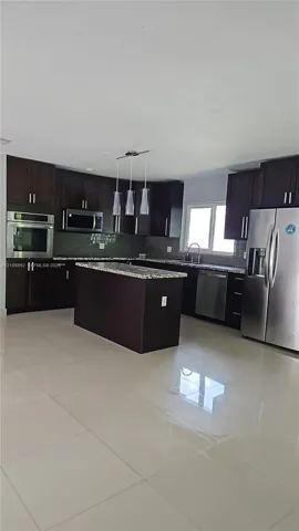 Kitchen featuring dark cabinetry, stone-surface countertops, central island, stainless steel appliances, and large-format tile flooring