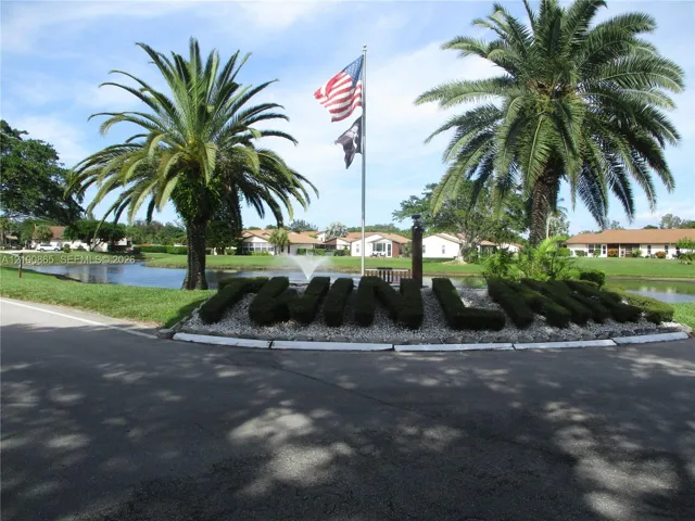 Community entrance featuring shaped shrubbery, palm trees, a central fountain, and a water feature