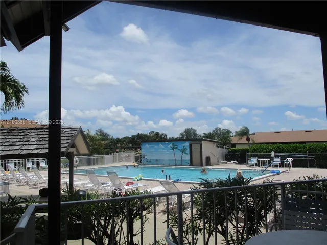 Outdoor swimming pool featuring a concrete deck and a perimeter metal fence with a shaded area