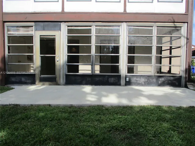 Enclosed patio featuring a concrete slab foundation, multiple horizontal louvered windows, and a glass-paneled entry door