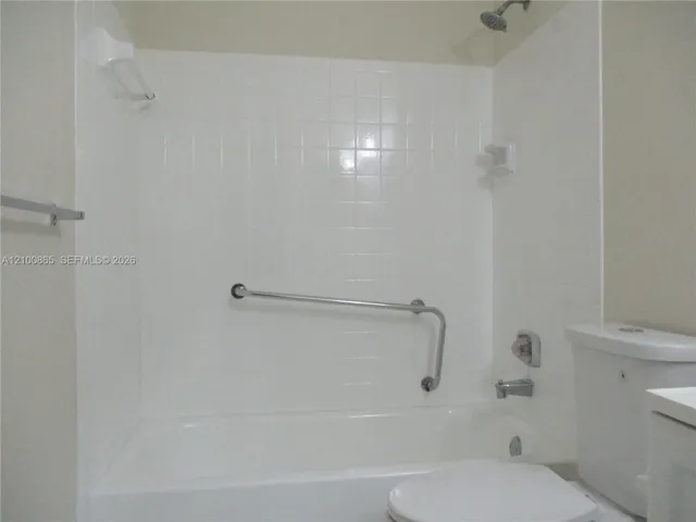 Guest Bathtub enclosure featuring white ceramic wall tiles, a built-in soap dish, a wall-mounted metal grab bar, and a standard metal shower head and faucet fixture