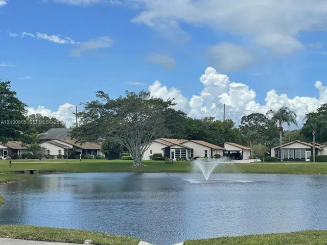 Waterfront pond featuring a central fountain, expansive manicured lawn, and mature trees