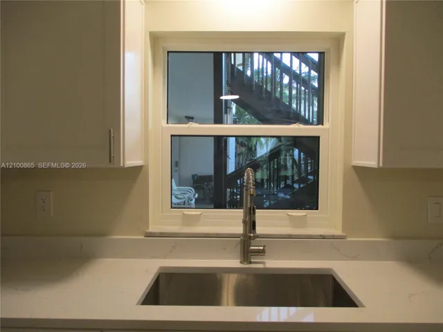 Stainless steel undermount sink with a high-arch pull-down faucet, white stone-finish countertops with integrated backsplash, and shaker-style cabinetry