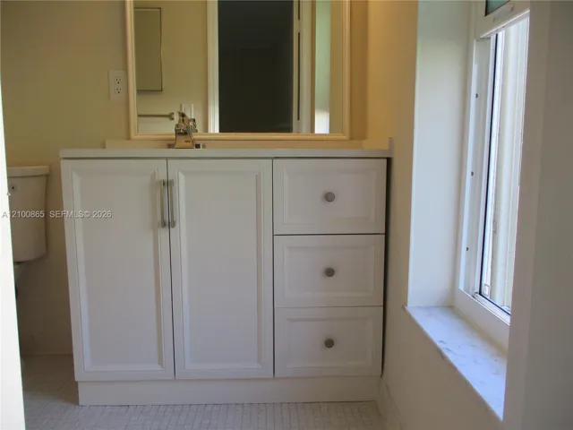 Master bathroom White cabinetry with brushed metal hardware, stone-top vanity, mirror with a white frame, and stone window sill