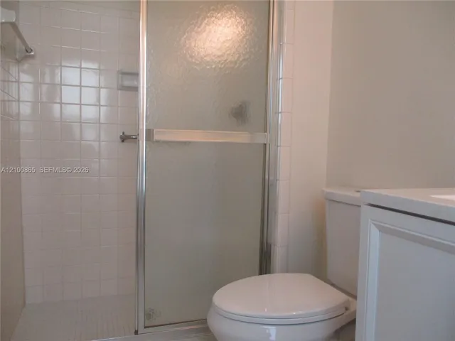 Master bathroom Shower stall with white square wall tile, semi-frameless textured glass door, and built-in soap niche, paired with a white vanity and porcelain commode