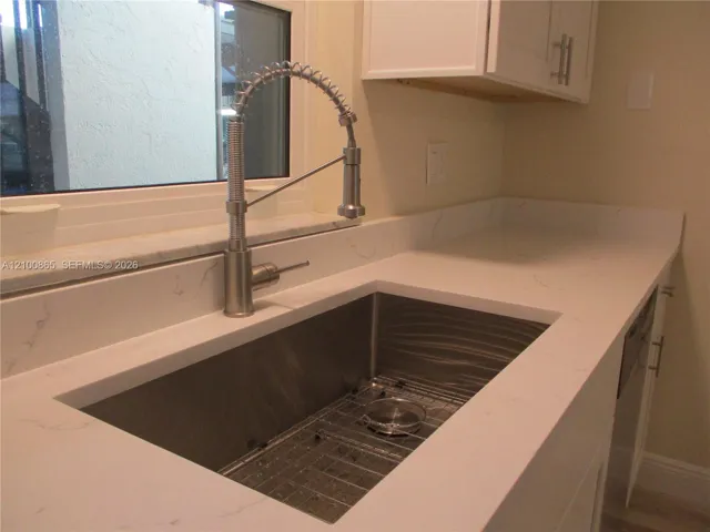 Undermount stainless steel sink with a protective grid, high-arc brushed nickel spring-neck faucet, and white stone-composite countertops with veining detail