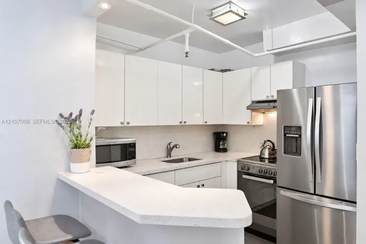 Kitchen featuring high-gloss white cabinetry, white stone countertops, stainless steel appliances, and integrated ceiling lighting