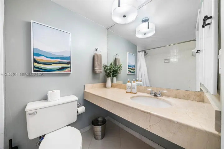 Wall-to-wall vanity with integrated stone-finish countertop, undermount oval sink, chrome dual-handle faucet, large-scale vanity mirror, and dual drum-style light fixtures