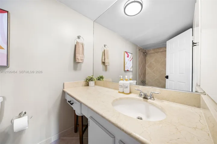 Bathroom featuring a vanity with a stone countertop, oval undermount sink, full-width wall mirror, and a tiled shower surround