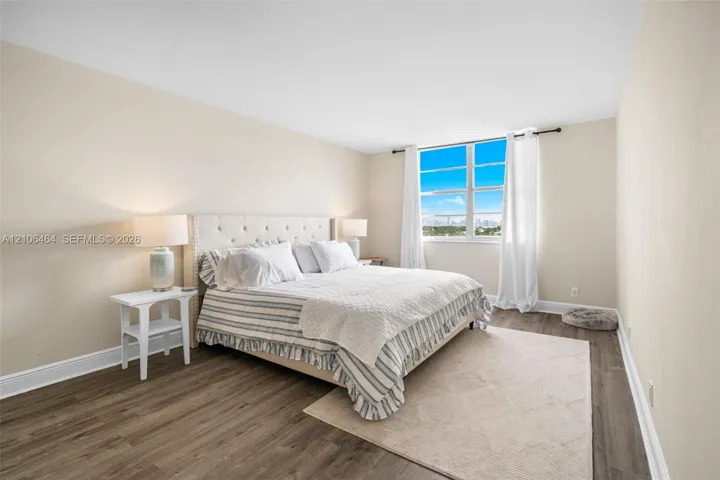 Neutral-toned bedroom featuring wood-finish flooring and large windows with natural lighting
