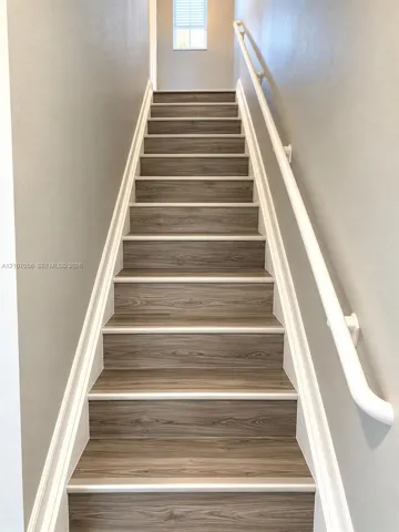 Staircase featuring wood-finish treads, white painted handrails, and neutral wall tones