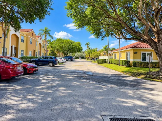 Multi-story stucco buildings featuring clay tile roofs, surface parking, and mature trees