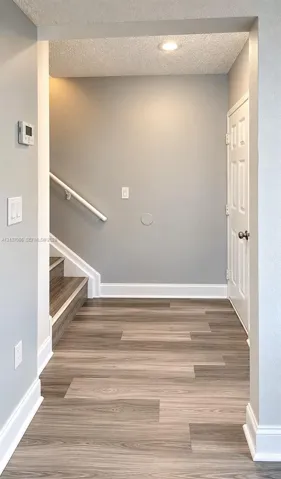 Entryway featuring wood-finish flooring, recessed ceiling lighting, a six-panel door, and a white handrail