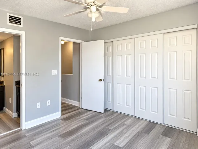 Room featuring wood-finish flooring, a white ceiling fan with integrated lighting, and a multi-panel sliding closet