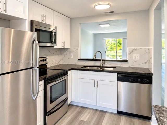 Kitchen featuring white cabinetry, stainless steel appliances, dark countertops, a stone-patterned backsplash, and wood-finish flooring