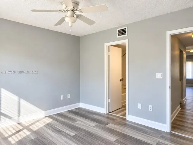 Bright, light-filled bedroom featuring gleaming wood-finish flooring, neutral gray walls, and a ceiling fan with integrated lighting