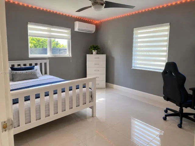 Large-format tile flooring, wall-mounted ductless air conditioning unit, ceiling fan with integrated lighting, dual-pane windows with banded roller shades