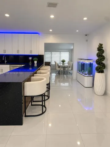 Modern kitchen featuring a breakfast bar with stone-finish countertops, white cabinetry, integrated under-cabinet lighting, and polished large-format tile flooring