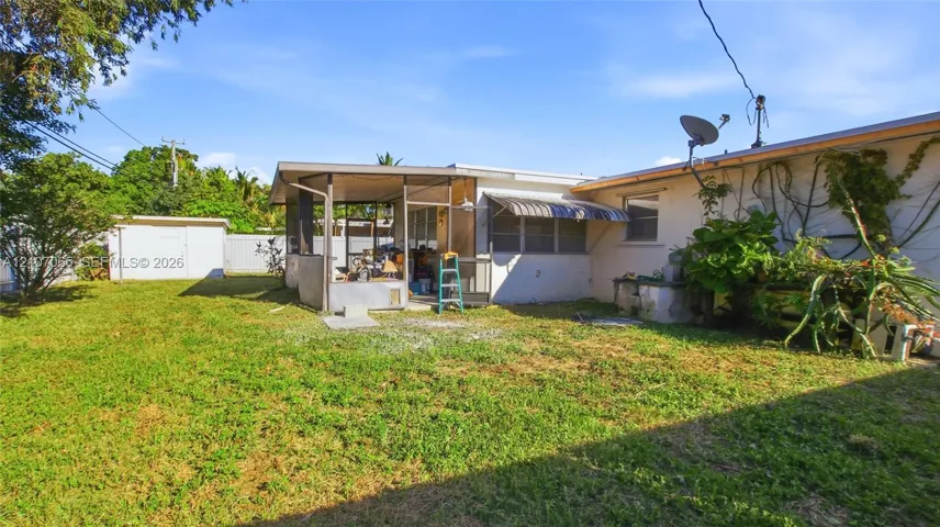 Rear exterior featuring a screened-in porch, metal window awnings, and a detached storage shed on a fenced lot