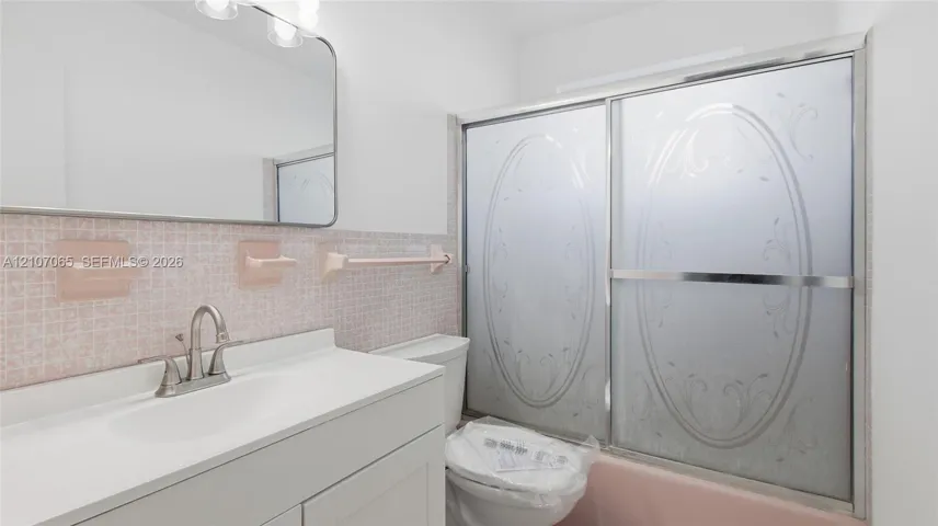 Bathroom featuring a solid-surface countertop, integrated basin, wall-mounted mirror, and a shower-tub combination with etched sliding glass doors and decorative mosaic tile backsplash