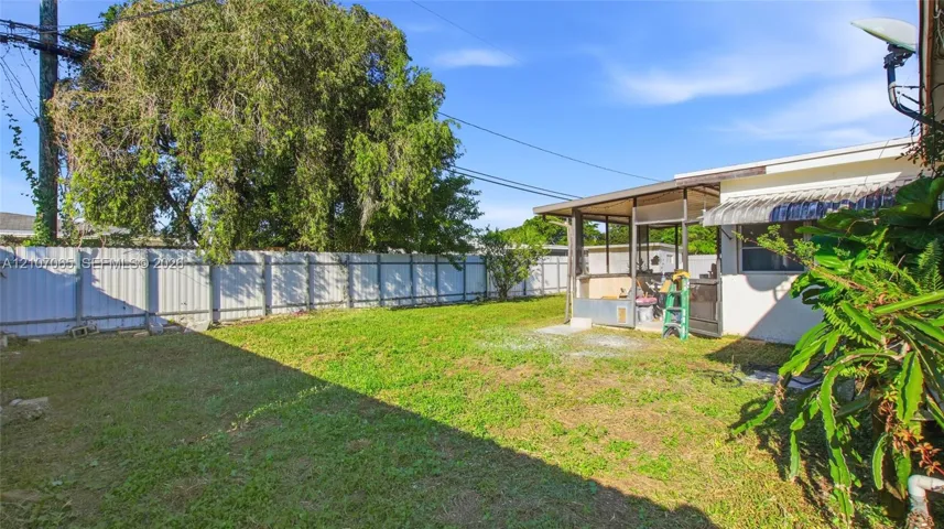 Backyard featuring a grass lawn, metal privacy fencing, and an attached screened-in porch with a metal awning