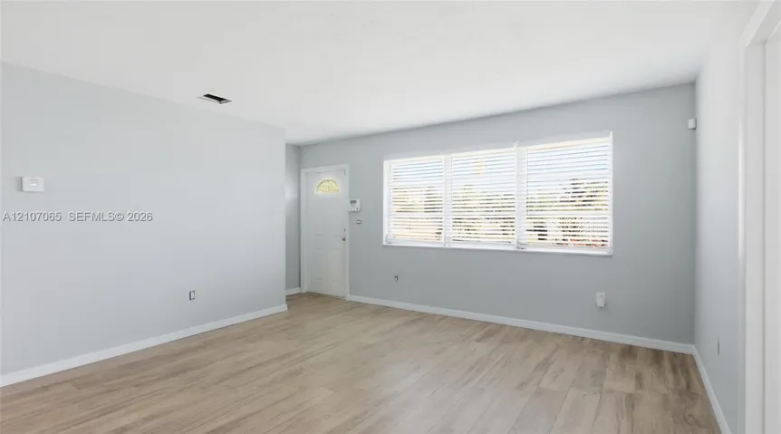 Neutral interior with light-toned wood-finish flooring, white walls, and a large triple-pane window with installed horizontal blinds