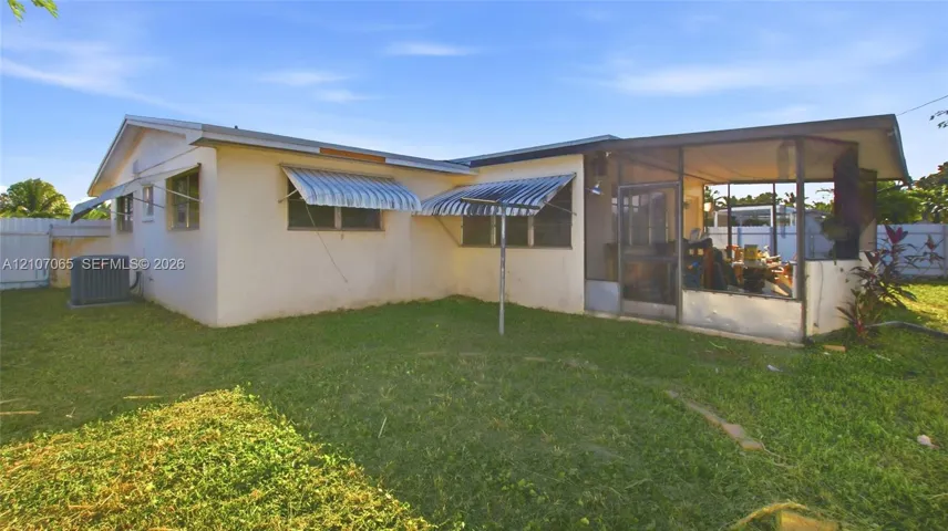 Exterior featuring a screened-in lanai, light-colored stucco siding, metal window awnings, and a fenced backyard
