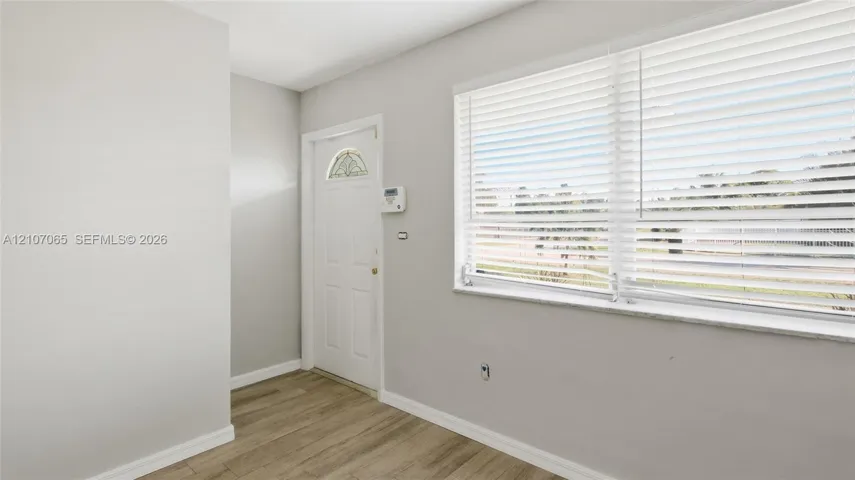 Bright corner room featuring wood-finish flooring, neutral wall finishes, and dual windows with horizontal blinds providing natural light and privacy control